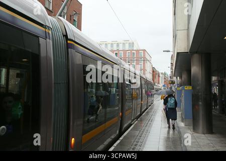 Dublin, Irlande - 19 septembre 2025 - le Luas Jervis Street s'arrête alors qu'un tramway part tandis qu'une femme avec un parapluie passe dans la ville de Dublin par un après-midi couvert humide dans la capitale irlandaise Banque D'Images