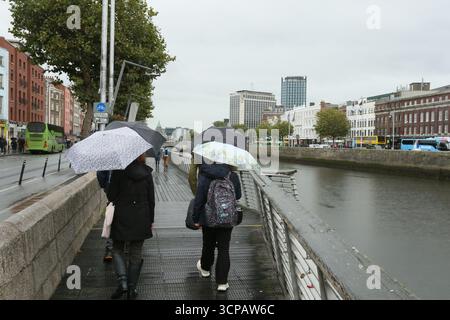 Dublin, Irlande - 19 septembre 2025 - les personnes avec des parapluies marchent sur la promenade le long de la rivière Liffey pendant les précipitations dans la ville de Dublin par un après-midi couvert humide dans la capitale irlandaise Banque D'Images