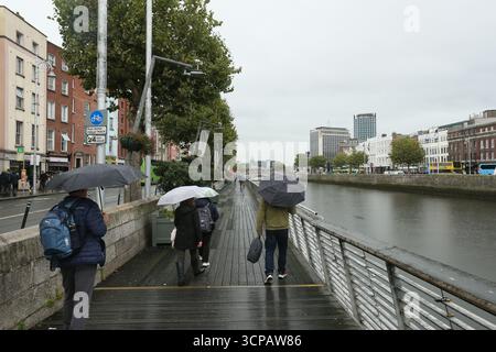 Dublin, Irlande - 19 septembre 2025 - les personnes avec des parapluies marchent sur la promenade le long de la rivière Liffey pendant les précipitations dans la ville de Dublin par un après-midi couvert humide dans la capitale irlandaise Banque D'Images