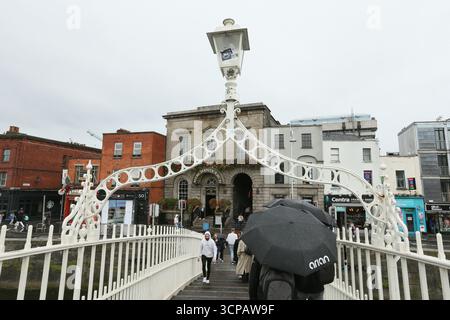 Dublin, Irlande - 19 septembre 2025 - les personnes avec des parasols marchent sur le pont Ha'Penny le long de la rivière Liffey pendant les précipitations dans la ville de Dublin par un après-midi couvert humide dans la capitale irlandaise Banque D'Images