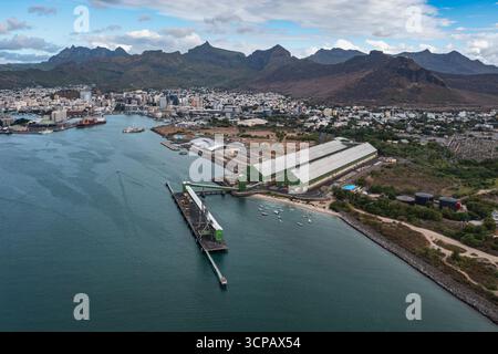 Vue aérienne des structures industrielles rencontrent la mer tranquille, contrastant avec le fond montagneux de la ville, Port Louis, Port Louis District, Maurice. Banque D'Images