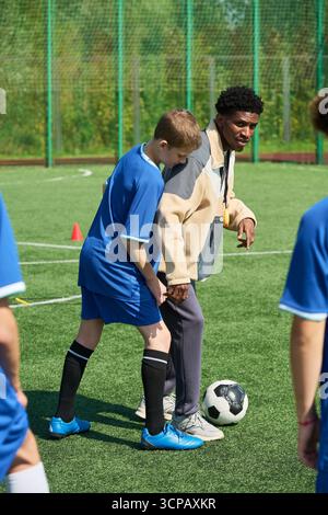 Garçon apprenant les compétences de football de Black Man Coach en plein air Banque D'Images