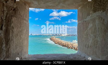 Alexandrie, Egypte - 13 février 2025 : vue sur la mer Méditerranée et la ville d'Alexandrie encadrée par une fenêtre en pierre ouvrant sur le Cita historique Banque D'Images