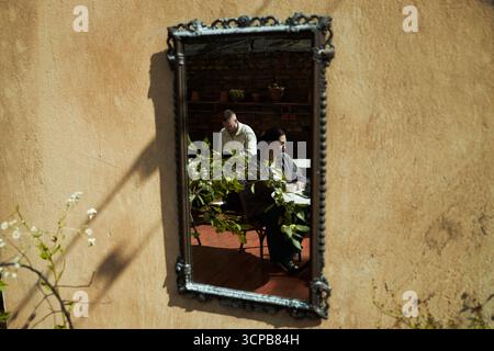 Homme d'âge moyen caucasien et femme d'âge moyen noire assis ensemble à table reflété dans un miroir mural orné, les deux axés sur la lecture ou l'écriture, cadre rustique intérieur Banque D'Images