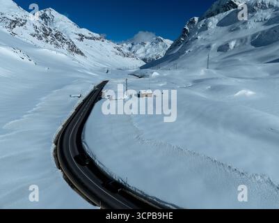 Vue aérienne d'une route sinueuse tranchant à travers la neige blanche et dure du col du Julier, sous le regard attentif des montagnes imposantes et déchiquetées, col du Julier, Grisons, Suisse. Banque D'Images