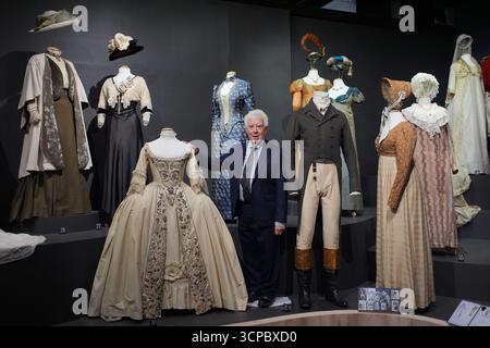 John Bright, créateur de costumes lauréat des Oscars et BAFTA, pose à côté de costumes exposés, dont (de gauche à droite) 1910 ensembles du film Howards End (1992), portés par Vanessa Redgrave et Emma Thompson ; une robe de mariée des années 1770 du film Frankenstein de Mary Shelley (1994), portée par Helena Bonham carter ; une robe des années 1880 (derrière, centre, bleue) du film Young Toscanini (1988), portée par Elizabeth Taylor; et 1810 costumes pour la série télévisée Pride and Prejudice de la BBC (1995), portés par Colin Firth, Anna Chancellor, Lucy Robinson, Jennifer Ehle et Alison Steadman ; et (à l'extrême droite) un mariage des années 1790 Banque D'Images