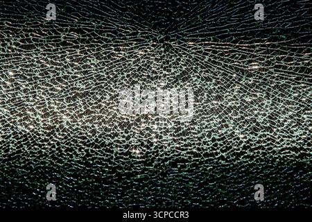 Gros plan d'une fenêtre en verre brisé montrant une bande complexe de fissures rayonnant à partir d'un point d'impact central. Les éclats dentelés réfléchissent la lumière en vert-W. Banque D'Images