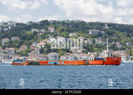 Istanbul, Turquie - 24 août 2024 : un grand cargo orange Neta glisse à travers l'eau libre du Bosphore avec une ville à flanc de colline d'arbres verts et blancs Banque D'Images