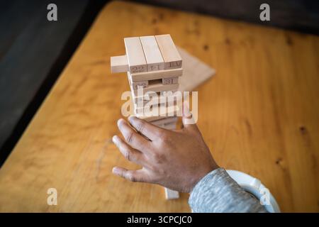 Homme indien pressant le bloc de la tour en bois sur la table en bois poli au café près de la tasse blanche Banque D'Images