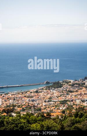 Une vue aérienne panoramique capture la ville côtière animée de Funchal, Madère, nichée entre des collines verdoyantes et le vaste océan Atlantique bleu. Le Banque D'Images