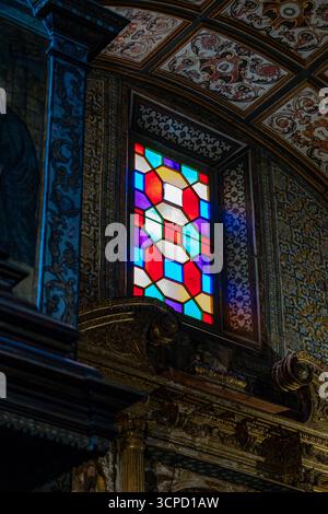 Un vitrail vibrant, avec des motifs géométriques dans les tons de violet, rouge, vert et bleu, illumine l'intérieur richement décoré d'un Banque D'Images