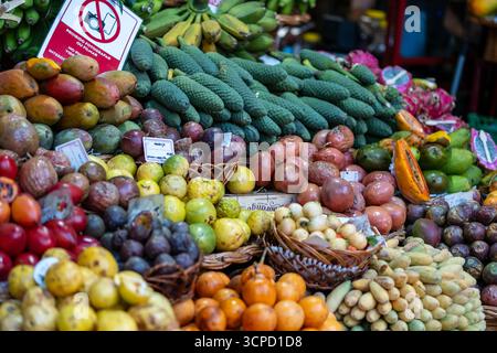 Une gamme vibrante de fruits tropicaux, y compris des bananes mûres, diverses mangues, fruits de la passion, et des monsteras uniques, sont méticuleusement exposés pour la vente a. Banque D'Images