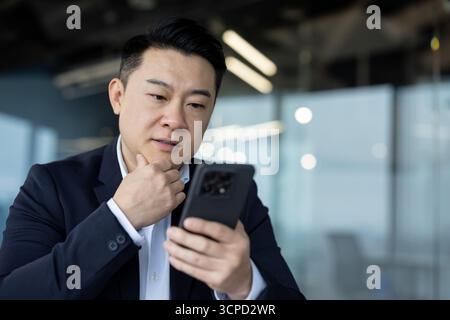 Photo en gros plan d'un jeune homme asiatique sérieux regardant attentivement son téléphone. Banque D'Images