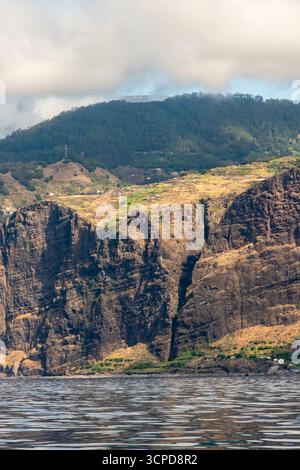 Un paysage côtier spectaculaire présente d'imposantes falaises plongeant dans l'océan, avec des collines en terrasses parsemées de petites maisons et de forêts luxuriantes sous-jacentes Banque D'Images