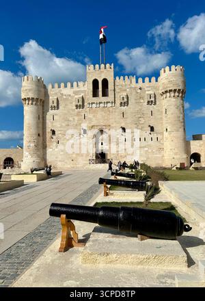 Alexandrie, Égypte - 13 février 2025 : visiteurs à la citadelle médiévale de Qaitbay forteresse avec drapeau égyptien et canons exposés. Banque D'Images