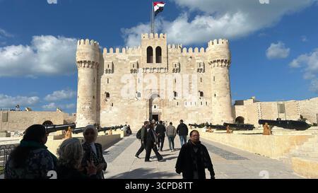 Alexandrie, Égypte - 13 février 2025 : visiteurs à la citadelle médiévale de Qaitbay forteresse avec drapeau égyptien et canons exposés. Banque D'Images