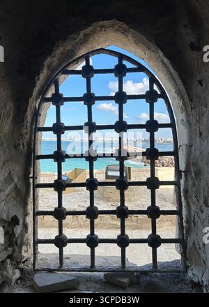 Alexandrie, Égypte - 13 février 2025 : fenêtre en pierre voûtée avec barres de fer à la forteresse Citadelle de Qaitbay surplombant la côte méditerranéenne. Banque D'Images