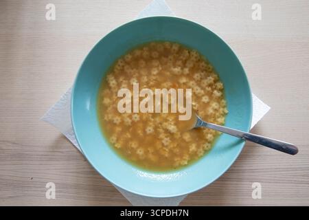 Bouillon clair maison avec de petites pâtes en forme d'étoile servies dans un bol bleu. Soupe chaude réconfortante avec une cuillère, repas simple traditionnel, vue rapprochée sur w Banque D'Images