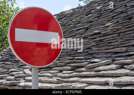 Un panneau circulaire rouge d'interdiction d'entrée se dresse à côté d'un toit de pierre empilé en plein jour, transmettant interdiction et sécurité. Idéal pour les sujets sur les règles de la route, Banque D'Images