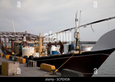 des hommes sur un boutre amarrés au port de sur dhow chargeant des marchandises au sultanat de sur oman Banque D'Images
