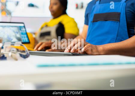 Travailleur afro-américain ajuste les paramètres industriels pour la production d'énergie solaire, travaillant dans une usine de fabrication de haute technologie. Technicien analysant les données techniques lors de la configuration du pc. Gros plan. Banque D'Images