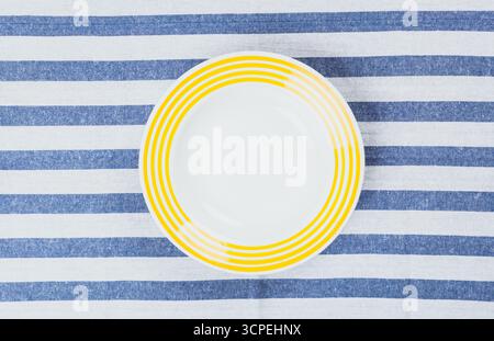 Assiette vibrante à rayures jaunes placée sur une nappe rayée bleue et blanche Banque D'Images