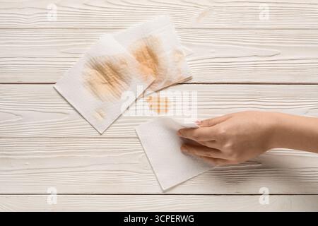 Femme essuyant le café renversé avec des serviettes en papier sur fond de bois blanc Banque D'Images