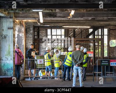 Les visiteurs portant des casques et des gilets de sécurité se rassemblent à l'intérieur de l'ancienne salle de puits de mine de charbon lors de la Journée des monuments ouverts sur le site patrimonial de Be-MINE Banque D'Images