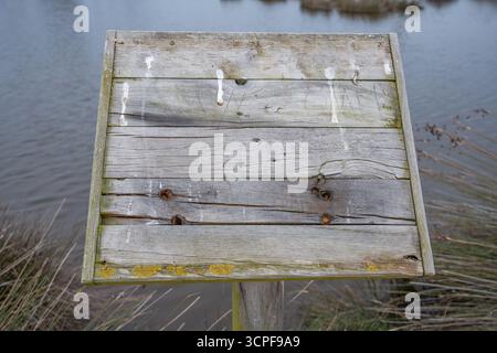 Panneau de signalisation en bois vierge altéré par un lac calme ou une zone humide le jour d'automne Banque D'Images