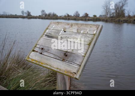 Panneau de signalisation en bois vierge altéré par un lac calme ou une zone humide le jour d'automne Banque D'Images