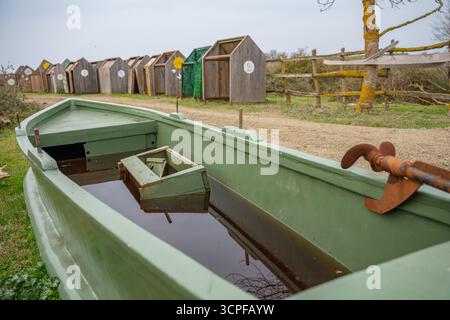 Vieux bateau de pêche vert avec gouvernail rouillé près du chemin rural. Bateau en bois vert inondé rempli d'eau, submergé. Campagne Banque D'Images