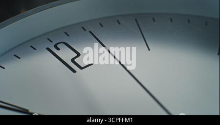 Macro gros plan de l'horloge murale minimaliste avec le numéro 12 sur le cadran et la seconde main en cours d'exécution. Élément de design moderne de l'intérieur. Concept de temps, ponctualité, attente, gestion du temps et style de vie Banque D'Images
