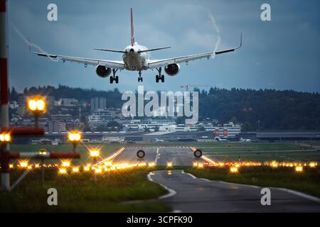 Avion commercial de passagers atterrissant sur une bande de piste éclairée d'aéroport. Au niveau du sol, arrière du point de vue du plan, sur le point de toucher des roues, telep Banque D'Images