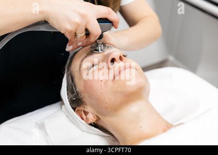 La cliente profite d'un soin de rajeunissement du visage RF Lifting dans un cadre de spa serein, mettant en valeur la technologie de soin de la peau avancée et l'ambiance apaisante Banque D'Images
