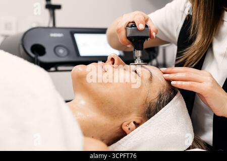 La cliente profite du traitement de rajeunissement facial RF lifting dans une clinique élégante, mettant en évidence l'équipement de pointe et une atmosphère sereine pour être efficace Banque D'Images
