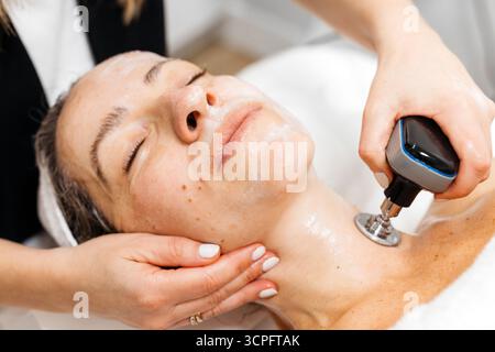 La cliente profite du traitement de rajeunissement facial RF Lifting, couchée confortablement sur le lit de traitement, entourée d'une atmosphère apaisante et d'un équipement de soins de la peau Banque D'Images