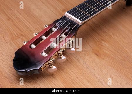 Une guitare avec une poupée noire et rouge repose sur une surface en bois. La poupée est ornée de quincaillerie en or et la guitare est un modèle vintage Banque D'Images