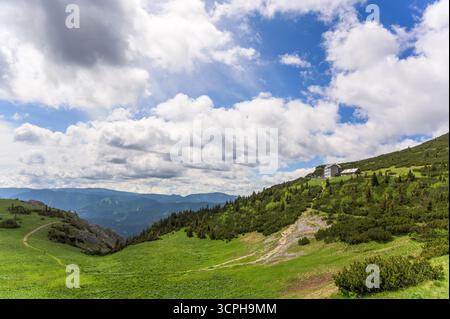 Une vue imprenable sur Rax Austria avec des collines verdoyantes avec de l'herbe luxuriante sous un ciel bleu vif orné de nuages blancs moelleux ; à l'arrière Banque D'Images