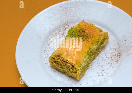 Doux de Baklava. Une tranche de baklava à la pistache turque servie sur une assiette blanche avec garniture à la cannelle. Dessert traditionnel avec pâtisserie feuilletée. Banque D'Images