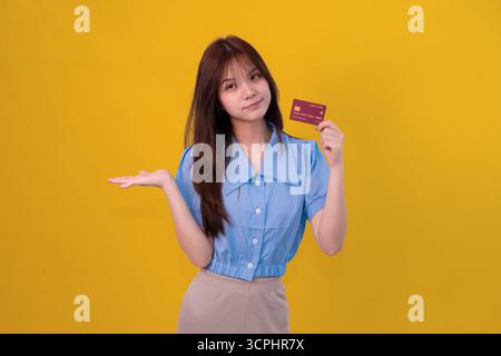 Jeune femme tenant la carte de crédit dans le fond de studio jaune lumineux pour le concept de shopping et de paiement Banque D'Images