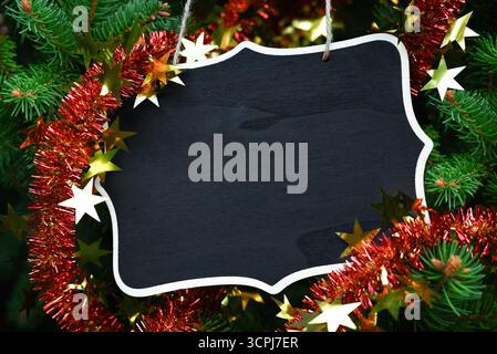 Tableau noir décoratif avec espace de copie, accroché à la ficelle parmi les branches d'épinette verte, décoré de guirlande rouge et d'étoile dorée. Banque D'Images