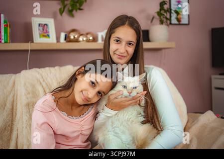 Soeurs souriantes avec chat de compagnie dans la maison confortable Banque D'Images