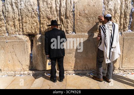 Jérusalem, Israël - 1er novembre 2019 : vue de figures pieuses en prière contre l'ancien mur occidental baigné de soleil, ses pierres altérées témoignent du temps, faisant écho à une dévotion chuchotée. Banque D'Images