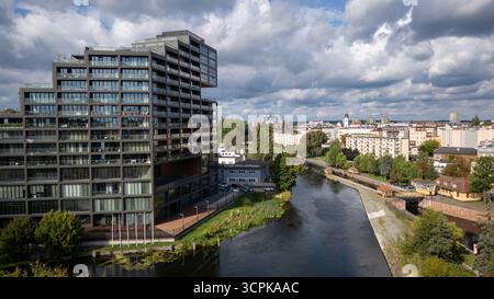 Vue aérienne du bâtiment moderne Mennica réfléchissant la lumière près de la rivière Brda sur fond de paysage urbain sous un ciel nuageux, Bydgoszcz, Województwo kujawsko-pomorskie, Pologne. Banque D'Images
