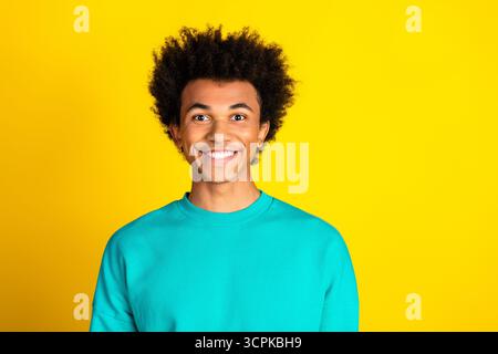 Jeune homme en sweat-shirt sarcelle souriant avec confiance sur un fond jaune vif mettant en valeur un style joyeux et positivité Banque D'Images