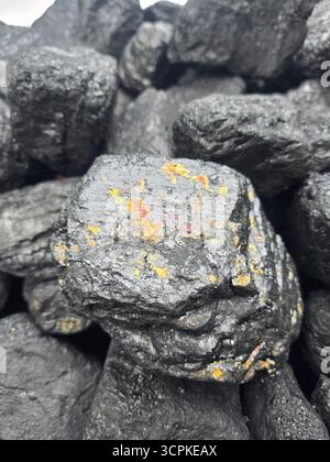 Gros plan d'un gros tas de morceaux de charbon noir brillants, dont une pièce présente des stries colorées, irisées et minérales. Banque D'Images