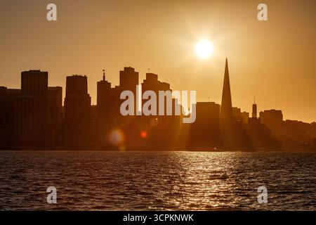 Le soleil se couche derrière les gratte-ciel de San Francisco, projetant une lueur dorée sur la ville et la baie. Banque D'Images Le soleil se couche derrière les gratte-ciel de San Francisco, projetant une lueur dorée sur la ville et la baie. Banque D'Images