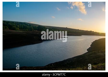 Lumière de l'heure d'or au-dessus du réservoir Baitings, révélant des niveaux d'eau significativement bas et des berges exposées en raison des conditions de sécheresse persistantes. Banque D'Images