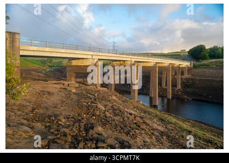 Bas niveau d'eau au réservoir Baitings, avec les fondations du pont normalement submergées exposées, mettant en évidence les conditions de sécheresse. Banque D'Images