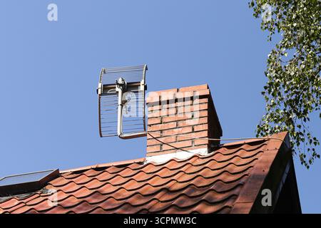 Toit avec tuiles rouges et antenne sur le dessus. Fond de ciel bleu clair. Détail de construction de la maison avec équipement de communication. Vue extérieure d'un bâtiment urbain Banque D'Images